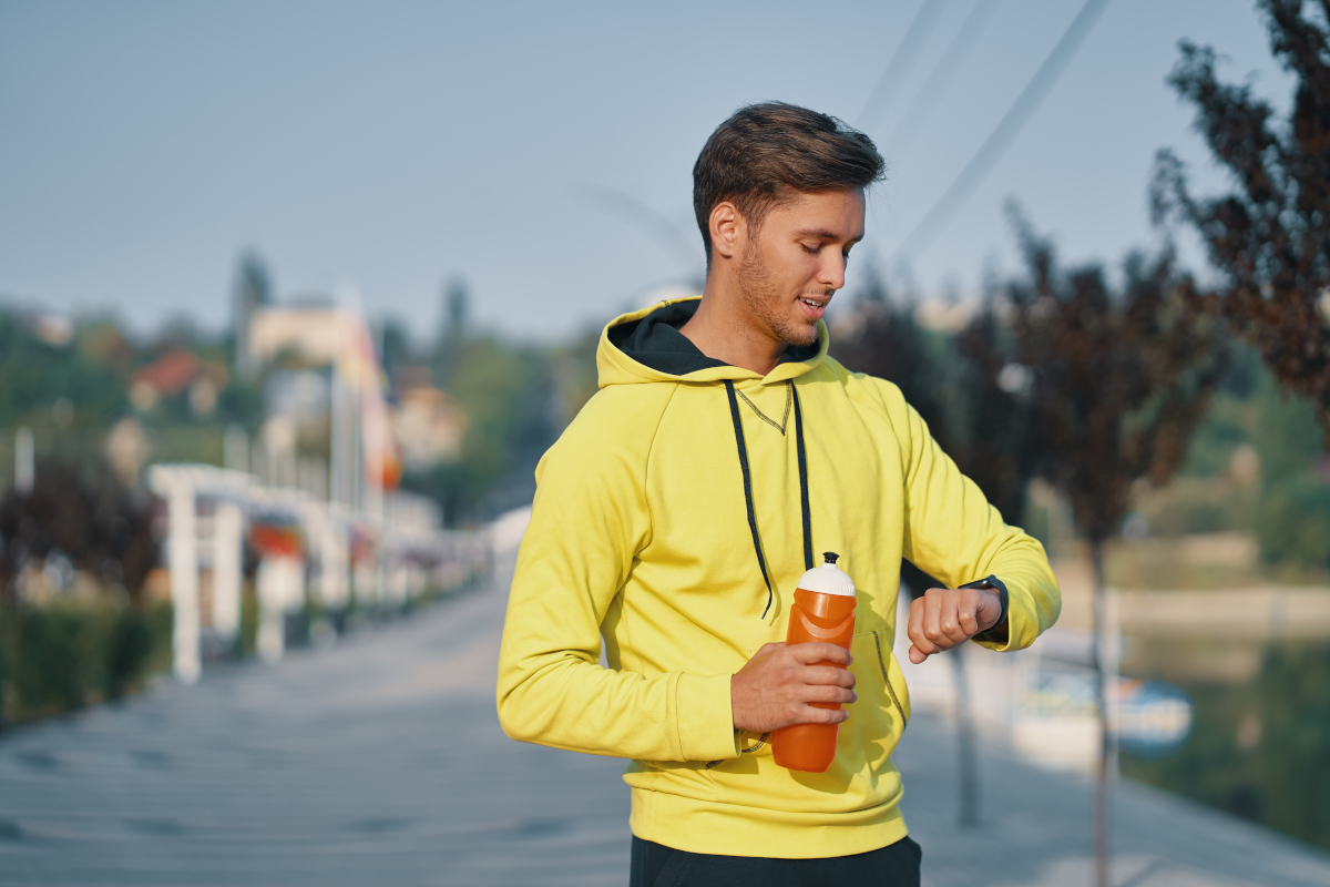 Sportsman with bottle of water is resting and checking his smart